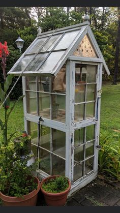 a small white greenhouse with two plants in the front and one potted plant next to it