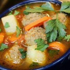 a blue bowl filled with meatballs, carrots and parsley on top of a table