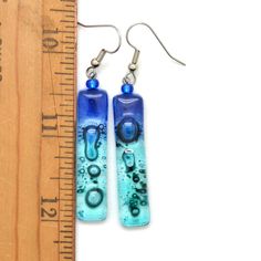 "Skinny cobalt blue, turquoise and aqua rectangle fair trade earrings. Some people might call these \"water colors\". Light & fun. Each pair is individually cut and cooked in the kiln. Each pair will bubble just a little different making each pair one-of-a-kind. These are so light, you will not remember you had them on. Size: Dangle 1-5/8\", width 5/16\" Materials: Fused glass, glass beads, Surgical steel ear wires Made in Guatemala, Fair Trade Verified When you order a gift for someone, and Modern Blue Long Drop Jewelry, Blue Rectangular Earrings With Ear Wire, Blue Rectangular Earrings, Blue Hypoallergenic Glass Earrings, Blue Glass Earrings With Ear Wire, Modern Blue Long Drop Earrings, Blue Glass Earrings For Gift, Nickel-free Blue Glass Earrings, Nickel Free Blue Rectangular Jewelry