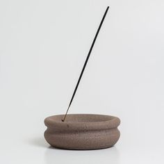 a stone bowl with a long black stick sticking out of it's center, sitting on a white surface