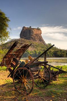 an old wooden cart sitting on top of a lush green field next to a mountain