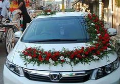 a white car with flowers on the hood parked in front of a horse drawn carriage