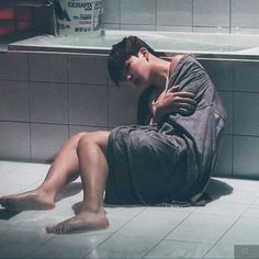 a man sitting on the floor in front of a bath tub with his head down