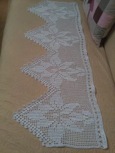 a white crocheted table runner sitting on top of a bed next to a pillow