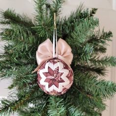 a christmas ornament hanging from the top of a pine tree with pink ribbon