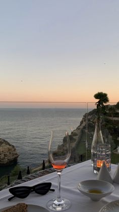 the table is set with wine and glasses on it, overlooking the water's edge