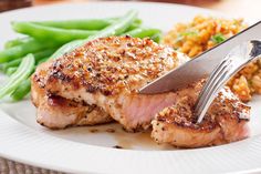 a plate with meat, rice and green beans on it is being cut by a knife