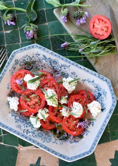 a plate filled with tomatoes and cheese on top of a green tile floor next to flowers