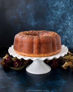 a bundt cake sitting on top of a white cake plate next to dried flowers