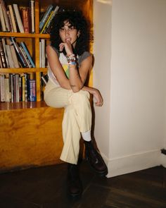 a woman sitting on top of a book shelf in front of a bookshelf