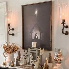 a mantle with candles and ornaments on it in front of a framed nativity scene