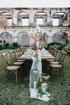 a long table set up with chairs and flowers in front of an old building on the grass