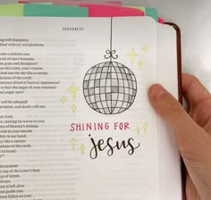 a hand holding an open book with the words shining for jesus on it and a globe hanging from strings