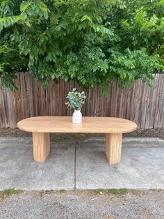 a wooden table sitting in front of a fence with a potted plant on top