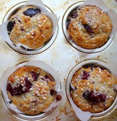 four muffins with blueberries and white sprinkles in tins