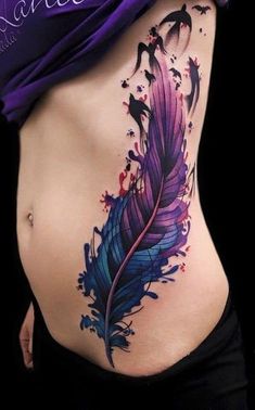 a woman's stomach with a purple and blue feather tattoo on the side of her belly