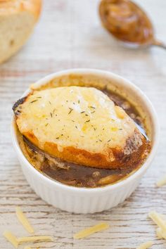 a bowl filled with food sitting on top of a wooden table next to some bread