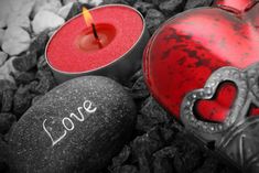 two red candles sitting next to each other on top of black rocks with the word love written on them