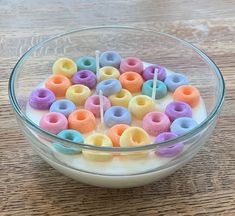 a glass bowl filled with lots of colorful doughnuts on top of a wooden table