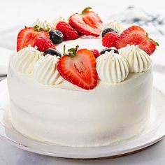 a white cake with strawberries and blueberries on top is sitting on a plate