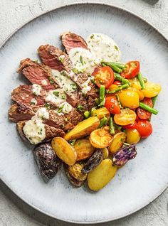 steak, potatoes and tomatoes on a white plate with ranch dressing in the middle is garnished with sour cream