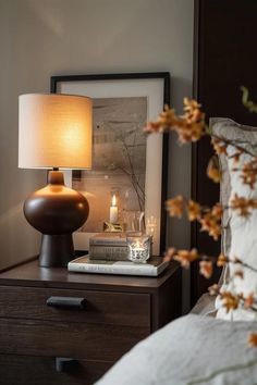 a bedside table with a lamp and books on it next to a framed photograph in a bedroom