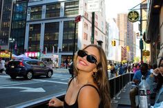 a woman standing on the side of a street next to tall buildings with cars and people