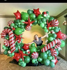 a woman standing in front of a christmas wreath made out of green and red balloons