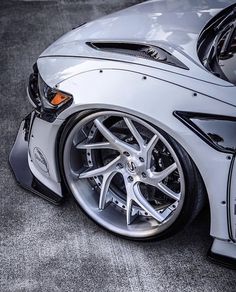 the front end of a silver sports car with chrome rims on it's wheels