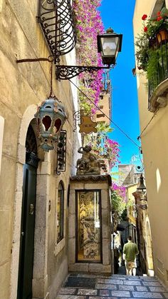 an alley way with flowers growing on the buildings and lanterns hanging from the side walls