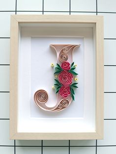 the letter j is made out of paper and decorated with flowers in a wooden frame