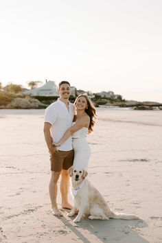 a man and woman are standing on the beach with their dog