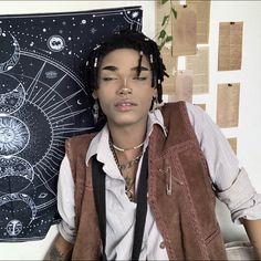 a young man with dreadlocks sitting in front of a wall decorated with astro signs