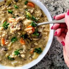 a person holding a spoon over a bowl of soup with meat and veggies