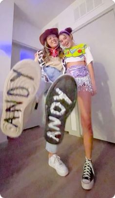 two girls are posing with their skateboards in front of the camera and one is wearing a hat