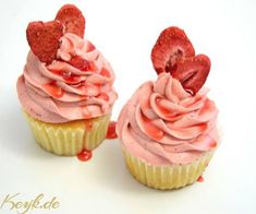 two cupcakes with pink frosting and strawberries on top are sitting side by side