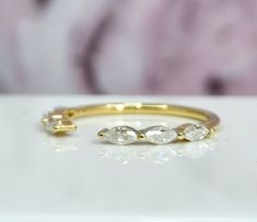 three stone ring sitting on top of a white surface with a pink flower in the background