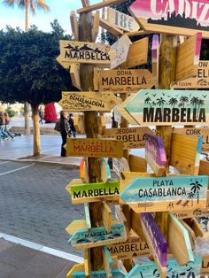 a wooden sign post with many different signs on it's sides and palm trees in the background