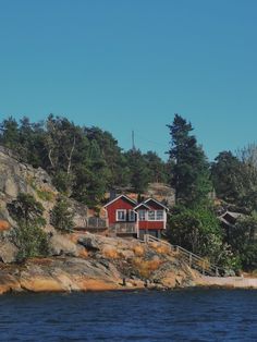 a red house sitting on top of a rocky cliff next to the ocean and trees