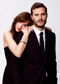 a man and woman posing for a photo in black suits with their arms around each other