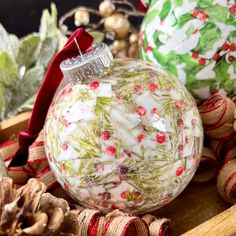 three christmas ornaments sitting on top of a wooden box next to pine cones and other holiday decorations