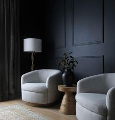 two chairs and a table in a room with black walls, rugs and curtains