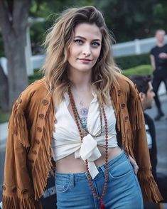 a woman wearing jeans and a brown jacket with fringes on it's shoulders