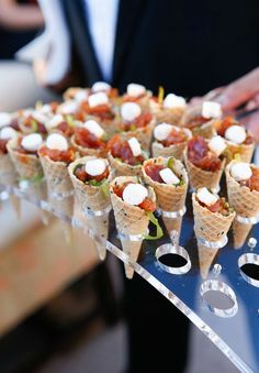 there are many small cones with toppings on the tray and one is holding an ice cream cone