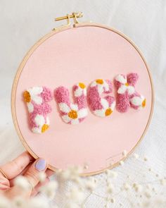 someone is stitching the word love in pink and white yarn with flowers on it