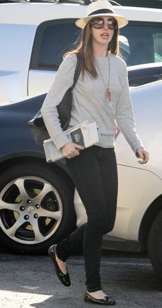 a woman wearing sunglasses and a hat walking past a car