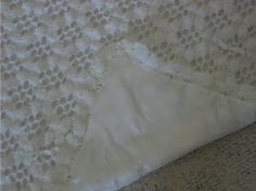 a piece of white lace sitting on top of a floor next to a bed sheet