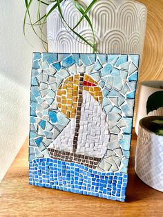 a mosaic tile with a sailboat on it sitting next to a potted plant