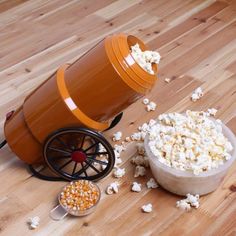 an orange popcorn machine sitting on top of a wooden floor next to a bowl of popcorn