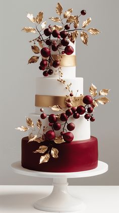 a three tiered cake with gold leaves and berries on top